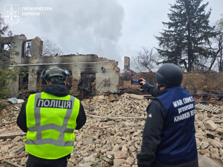 Два чоловіки в спеціальному одязі оглядають зруйновану будівлю та фіксують наслідки.