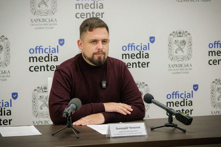 Чоловік у вишиванці сидить за столом із мікрофонами та табличкою Gennadiy Chekunov.