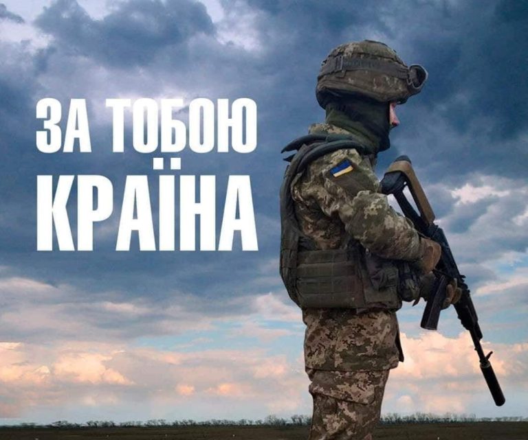 Український військовий у камуфляжі та з автоматом готовий до дії на тлі хмарного неба із гаслом 