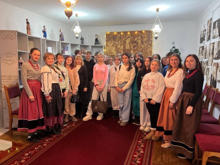 Жінки у вишитих національних українських костюмах та декілька чоловіків стоять у приміщенні бібліотеки разом з організаторами і учасниками заходу.