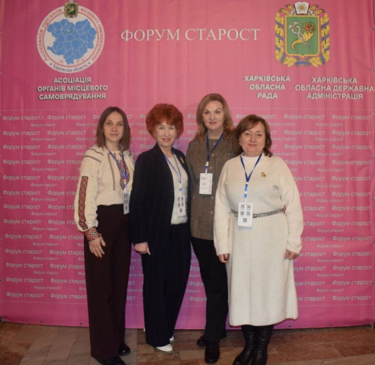 Чотири жінки у форменних бейджах стоять перед великим рожевим баннером із написом українською мовою 