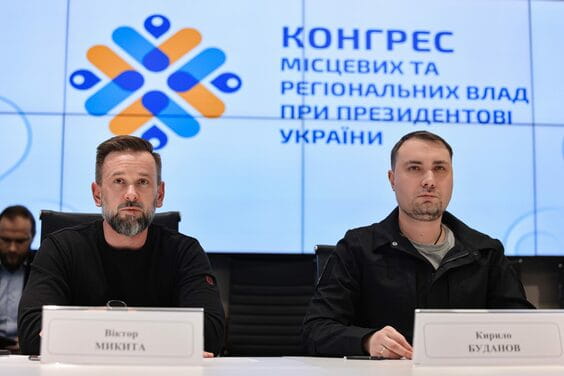 Два чоловіки сидять за столом із табличками імені на Конгресі місцевих та регіональних влад при Президентові України.