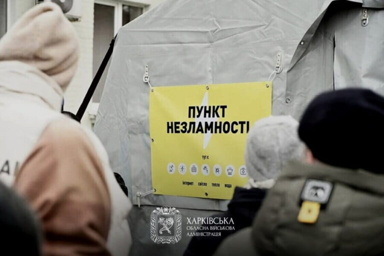 Пункт незламності, позначений жовтим знаком із чорним текстом російською мовою та іконками послуг, розташований біля входу в сірий намет, до якого звернені люди в зимовому одязі.