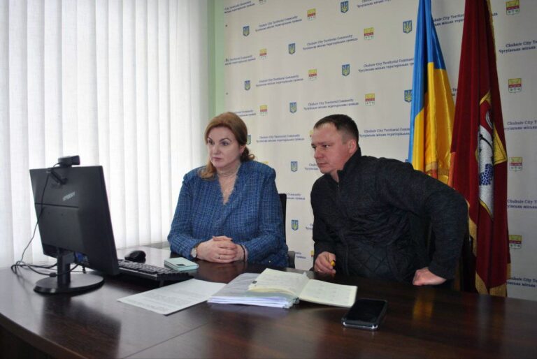 Жінка та чоловік сидять за столом і дивляться на монітор комп'ютера, поруч лежать документи та телефон.
