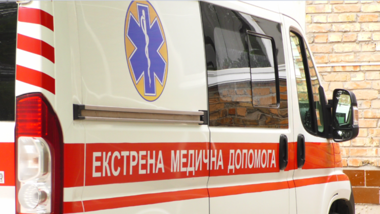 Біла машина швидкої допомоги з червоними смугами та написом 