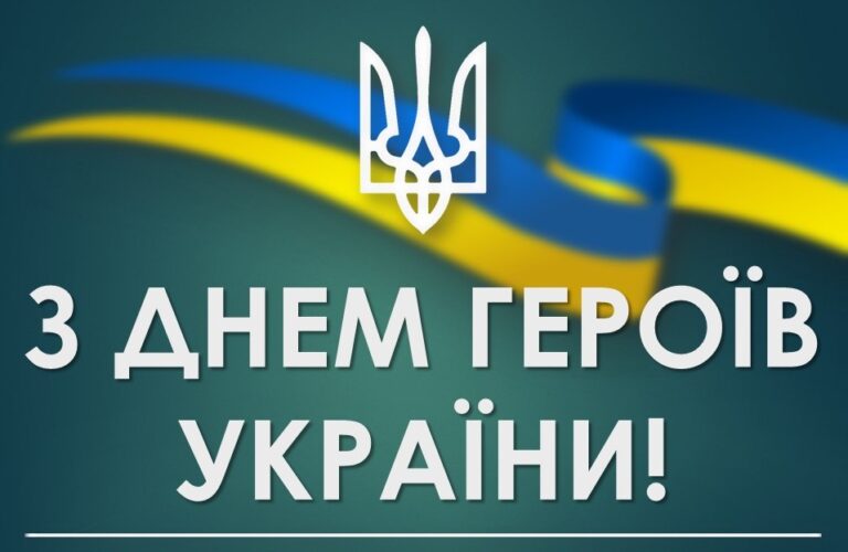 Білий тризуб і двічі по два крапки над літерою і на темно-зеленому тлі з жовто-блакитною стрічкою та написом українською мовою З ДНЕМ ГЕРОЇВ УКРАЇНИ.