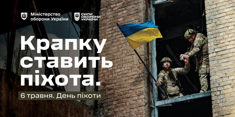 Два військовослужбовці в камуфляжі, один з яких допомагає іншому вилізти з вікна будівлі з пошкодженою цегляною стіною та українським прапором.