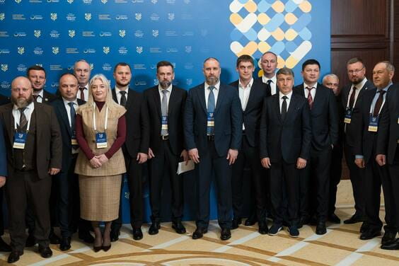 К група людей у діловому одязі та ідентифікаційних картках біля стіни із логотипами.