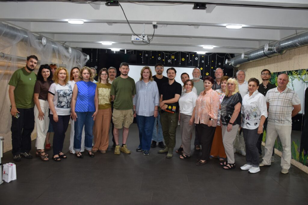 The user wants an alt text description for the provided image. The image shows a group of people standing together, likely for a group photo. I need to describe the main subject (the group) and their action (standing/posing). I need to mention any important text (none visible). The language must be Ukrainian. The format must be a single, concise sentence. No 