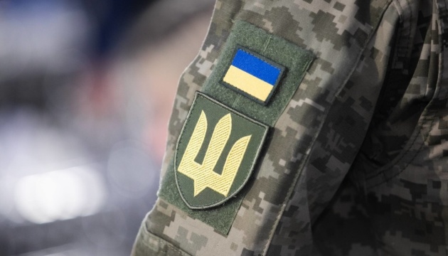 Український військовий у камуфляжній формі з нашивками українського прапора та емблемою Збройних сил України.