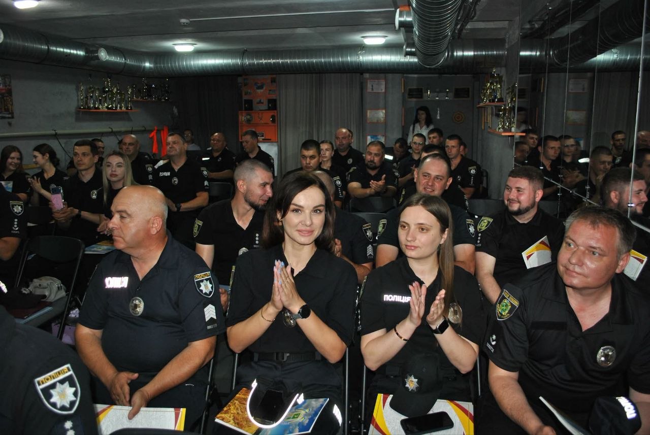 Кімната заповнена співробітниками поліції у формі, деякі з яких аплодують та дивляться на щось в передній частині кімнати.