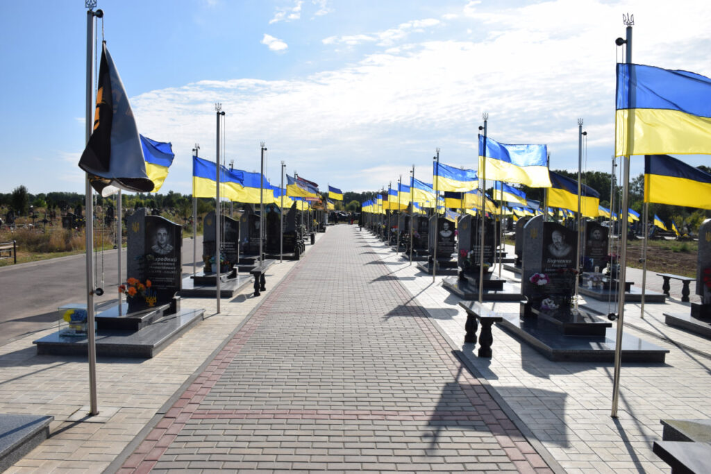 Ряди темних надгробків на цвинтарі, біля яких встановлені прапори України та військові прапори.
