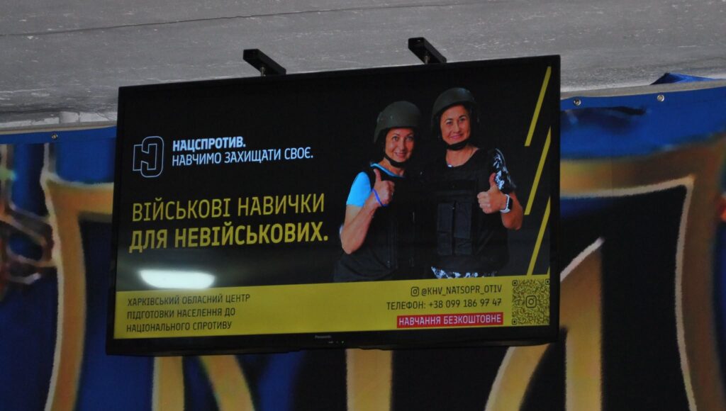 Рекламний екран Нацспротиву з написом «Військові навички для невійськових» та зображенням двох людей у тактичному спорядженні, які показують «клас».