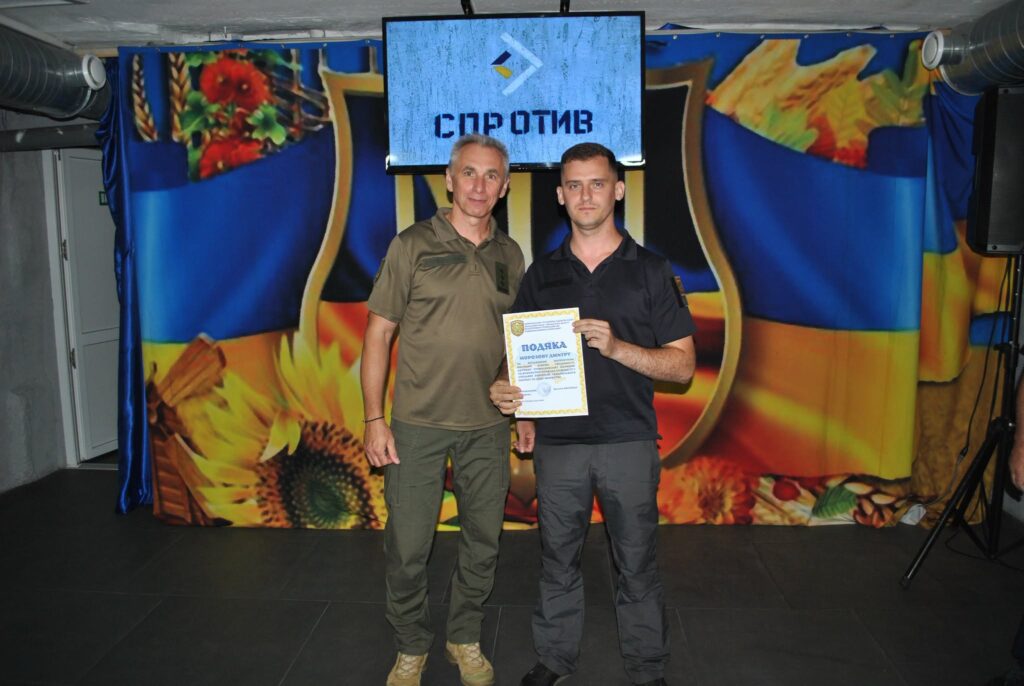 Два чоловіки стоять перед екраном із написом