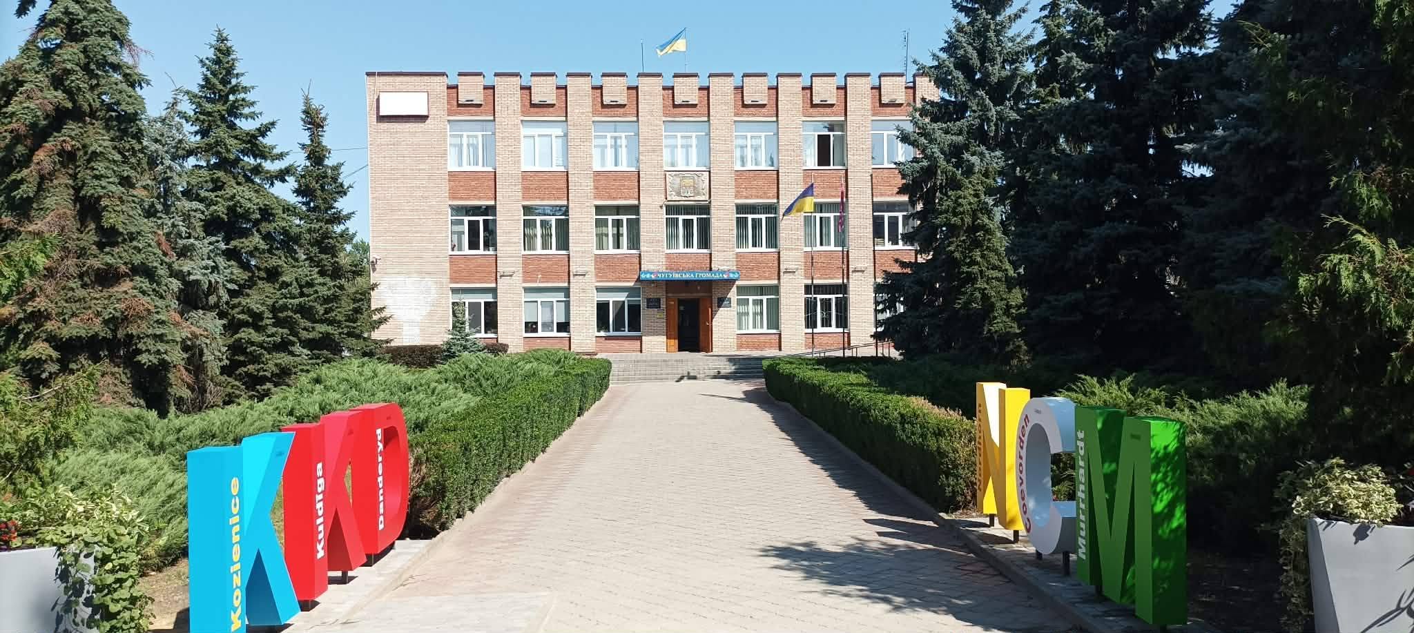 Цегляна будівля з українським прапором та великими кольоровими літерами KOD і NCM біля входу.