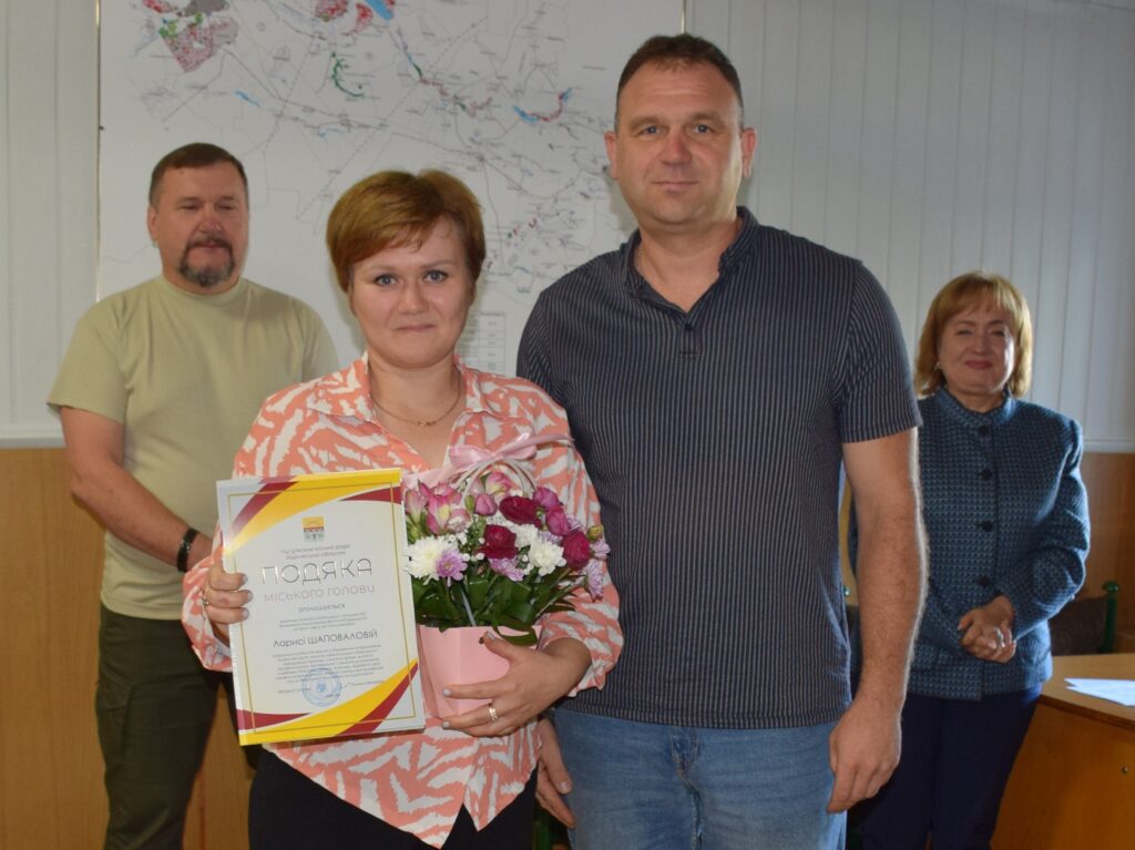 Жінка тримає букет квітів та подяку міського голови, отриману за багаторічну сумлінну працю.