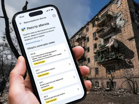 Людина тримає смартфон із відкритою сторінкою «Реєстр збитків» на тлі зруйнованого житлового будинку.