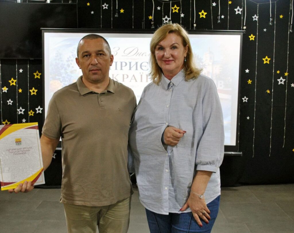 Чоловік тримає сертифікат «Членська міська культурна організація» поруч із жінкою на тлі банера з написом «ЄВРОПА».