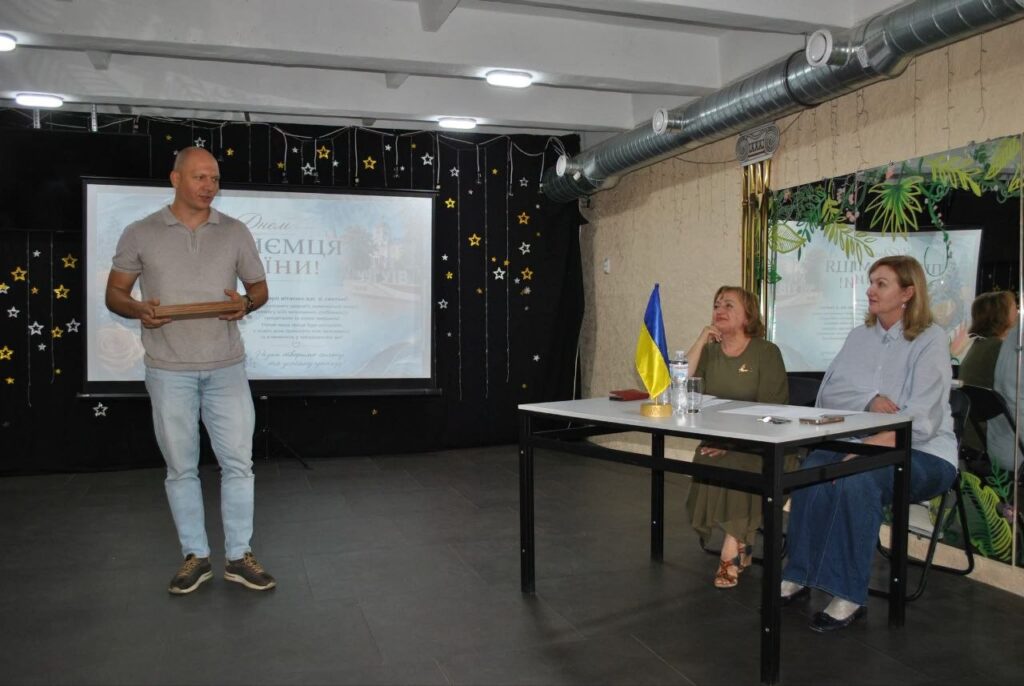 Чоловік тримає книгу під час презентації біля екрана з написом «Дякуємо, Україно!