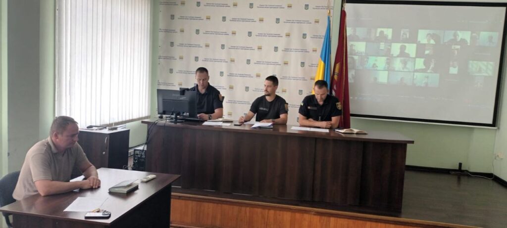Гібридне засідання, де учасники в залі та онлайн на екрані обговорюють питання.