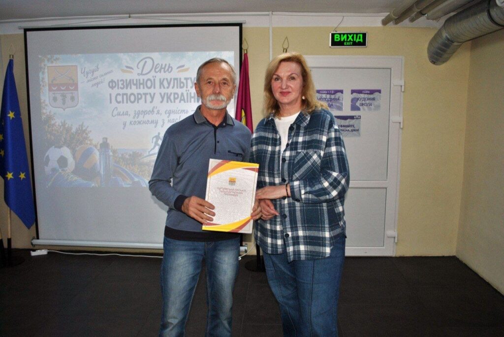 Чоловік і жінка тримають сертифікат на тлі банера з написом «День фізичної культури і спорту України».
