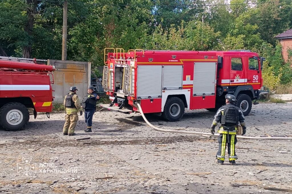 Пожежні у захисному спорядженні працюють біля червоного пожежного автомобіля з номером 50, розгортаючи пожежний рукав на ґрунтовій дорозі.