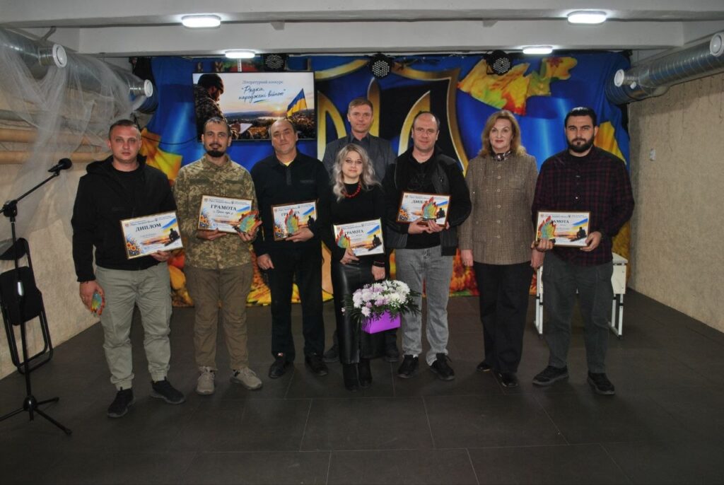 Група людей тримає грамоти та букет квітів на тлі банера з написом «Разом переможемо війну».