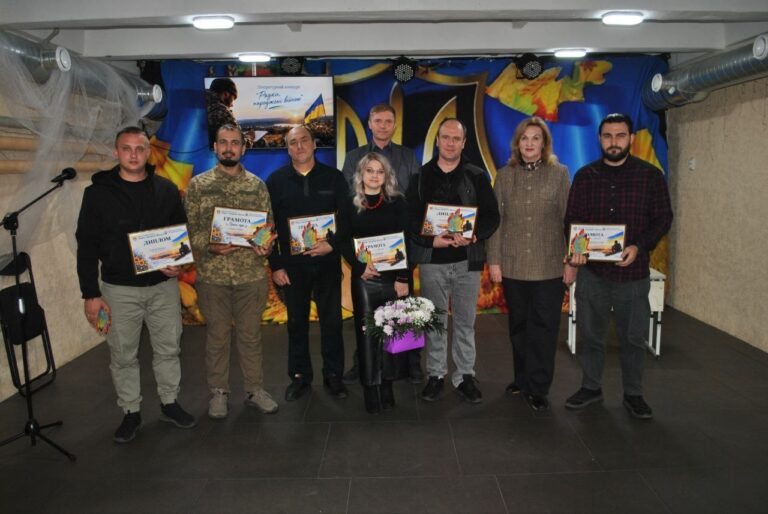 Група людей тримає грамоти та букет квітів на тлі банера з написом «Разом переможемо війну».