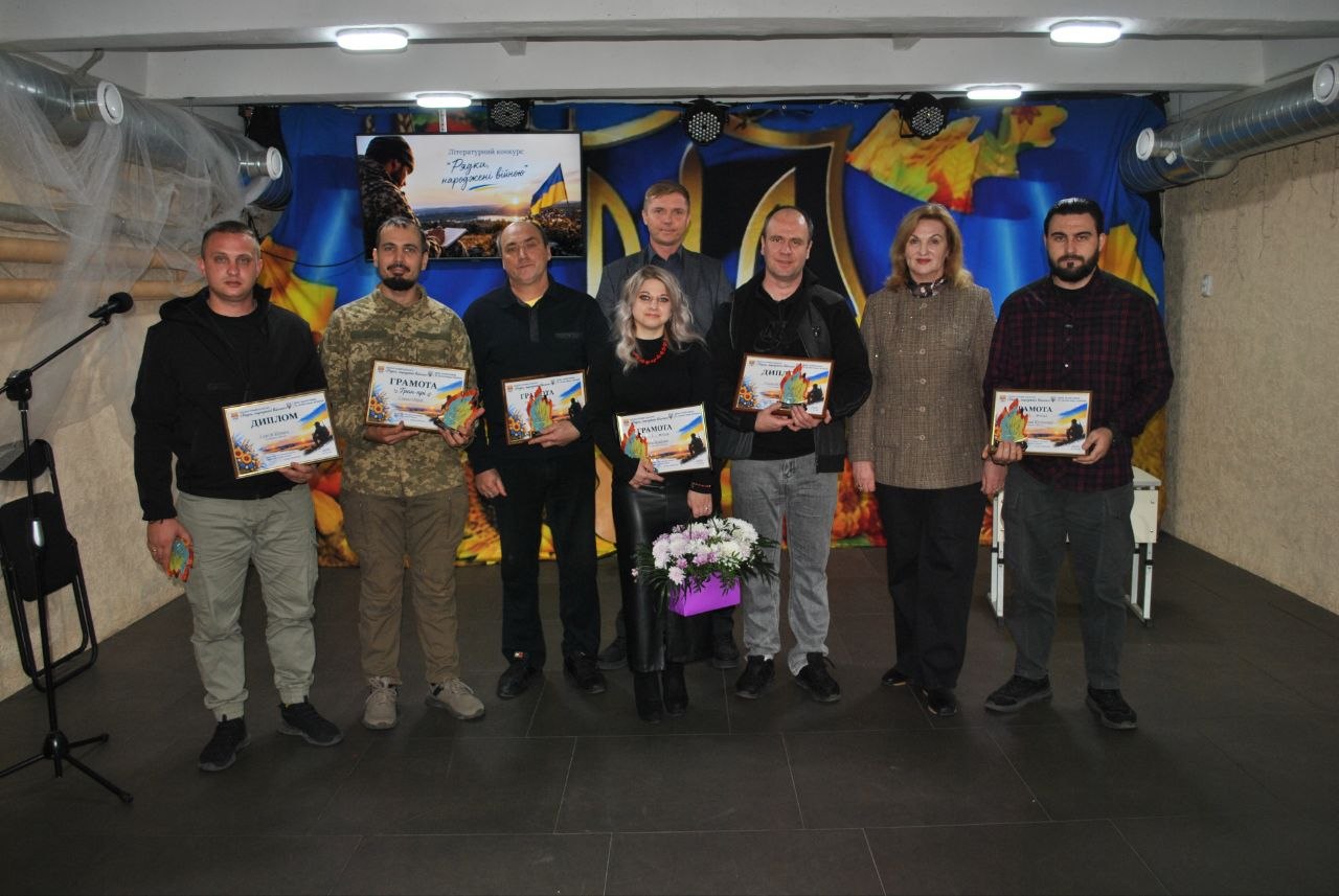 Група людей тримає грамоти та букет квітів на тлі банера з написом «Разом переможемо війну».