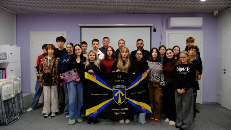 Група людей тримає прапор 57-ї окремої мотопіхотної бригади «Київська Русь» та нагороду.